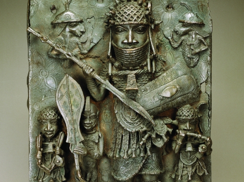 Bronze relief of a large figure holding long stick and smaller figures holding various items flanking him.