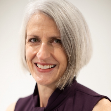 Woman with gray hair and sleeveless purple shirt smiles