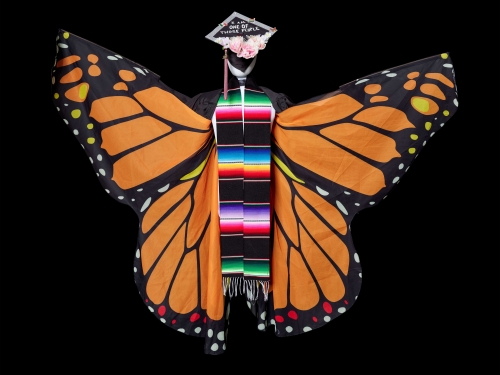 Person-sized monarch butterfly wings with a graduation cap and colorfully striped stole