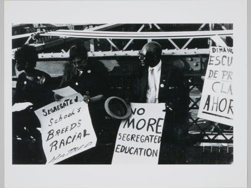 Black and white image of three people sitting with protest signs.