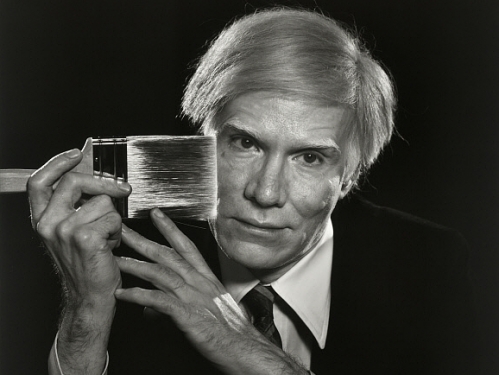 photograph of Andy Warhol holding a paint brush against his face